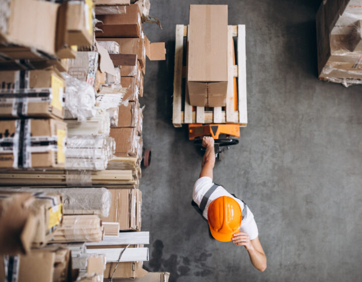 Magazijnmedewerker met fel-oranje helm treks karretje met doos